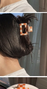 Detail of an orange checkered hair claw clip shown on a model and a white tray