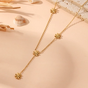 Detail of gold stainless steel Y-necklace with flower charms on pink beach background