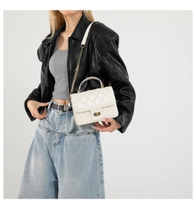 Détail d'un sac à bandoulière matelassé blanc avec chaîne dorée et fermoir pivotant