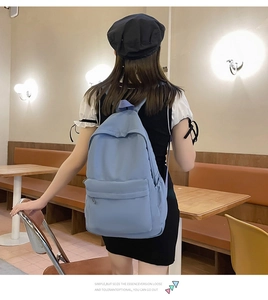 Rear view of a light blue minimalist backpack worn in a cafe setting, showing large capacity