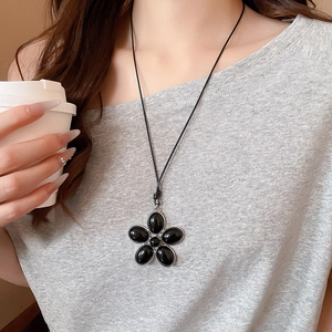 Detail of vintage oval flower pendant necklace on a grey sweater with white coffee cup