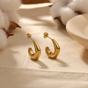 Close-up of gold-plated stainless steel U-shaped earrings on beige linen fabric background