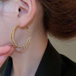 Close-up of double-layered bamboo style gold hoop earrings worn on a model ear