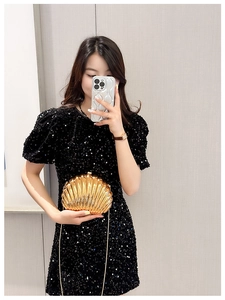 Detailed view of a gold shell-shaped clutch bag paired with a black sequin dress