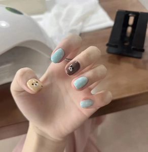 Detail of short round cartoon bear press-on nails with blue polka dots and glossy finish