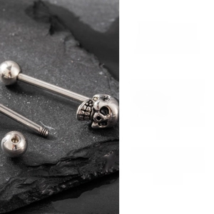 Detailed macro view of a silver stainless steel skull barbell piercing on a dark stone
