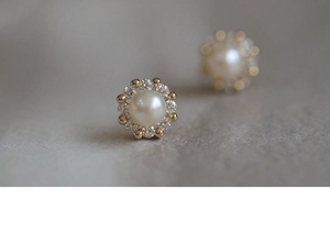 Macro shot of silver pearl stud earrings with sparkling zircon halo and golden metal base
