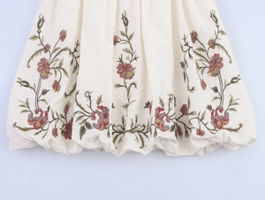 Close-up of intricate floral embroidery on white cotton fabric with pleated hem detail