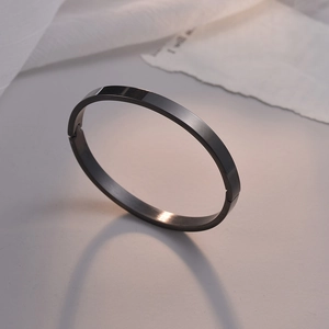 Brazalete minimalista de acero inoxidable negro pulido con cierre sobre fondo estético