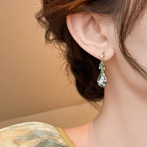 Close-up of elegant teardrop earrings with green enamel and pearls on model