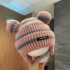 Detail of pink and gray striped knit baby hat with earflaps and cute pom-pom bear ears