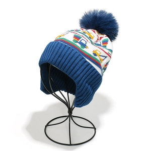Detail of children knit hat with fluffy blue pompom and colorful construction truck pattern