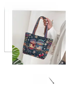 Detailed embroidery of owls and snowflakes on blue canvas tote with woven handles