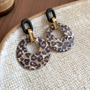 Close-up of retro leopard print acrylic hoop earrings with black matte studs on a beige tray