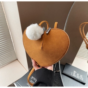 Detail der herzförmigen braunen Wildledertasche mit weißem Pelz-Bommel und Metallreißverschluss