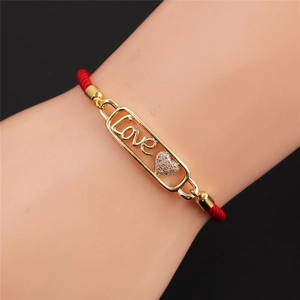 Dettaglio del bracciale in corda rossa con ciondolo Love dorato e cuore di pietra scintillante