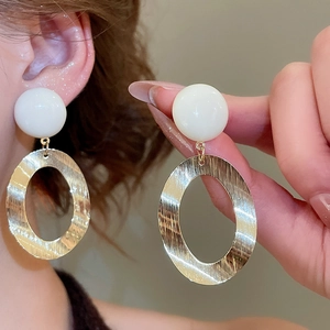 Detail of large oval brushed gold metal earrings with white resin beads on a model
