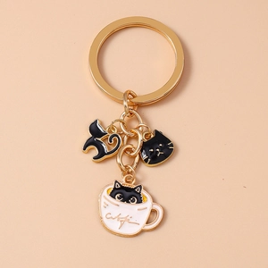 Close-up of metal keychain featuring black cat silhouettes and a white enamel Cafe coffee cup