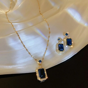 Detailed view of luxury gold jewelry set with emerald blue stones on white silk