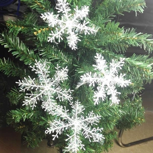 Close-up of three white glittery snowflake ornaments hanging on green Christmas tree branches
