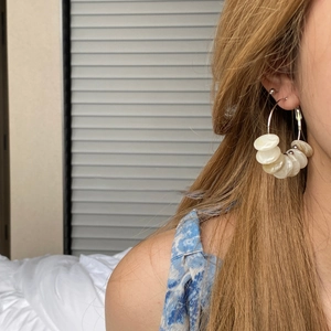 Close-up of model wearing geometric gold hoop earrings with white shell beads in detail