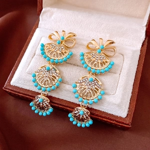 Détail de boucles d'oreilles vintage dorées avec éventail et perles bleues dans un écrin