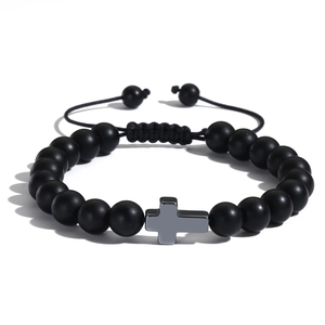 Dettaglio del bracciale intrecciato con perle nere opache e ciondolo a croce