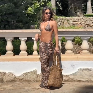 Three-piece leopard print bikini set featuring a wrap skirt and beach bag in a resort setting