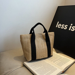 Detail of hand-woven straw tote with black canvas straps and reinforced bottom edges