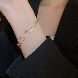 Detail of double-layer gold plated bracelet with pink and green beads on a wrist