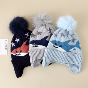 Close-up of three knitted winter hats with shark patterns and fluffy faux fur pom-poms