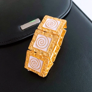 Macro detail of vintage gold bracelet with white enamel inlay and spiral metal texture