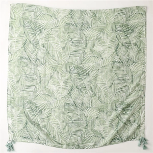 Detail of bohemian scarf with green leaf pattern and decorative tassels on soft fabric