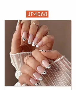 Detail of short almond press-on nails with French white tips and black polka dot pattern
