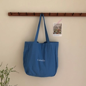 Detailansicht einer blauen Canvas-Tasche mit weißem Camellia-Schriftzug an einer Wand