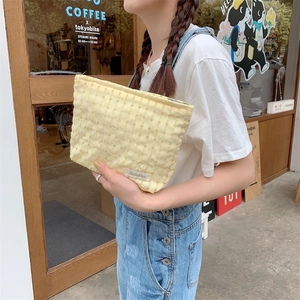 Close-up of yellow checkered fabric makeup bag held by a person in a lifestyle setting
