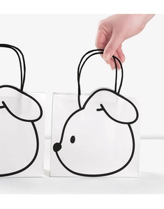 Close-up of minimalist white paper gift bag with cute cartoon dog print and black handles