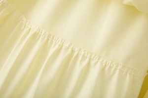 Detail of delicate stitching and ruched texture on light yellow tiered skirt