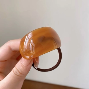 Macro view of a curved amber acetate hair tie with a flexible dark brown elastic band