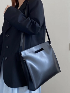 Detail of minimalist black leather tote bag worn by model over shoulder for commute