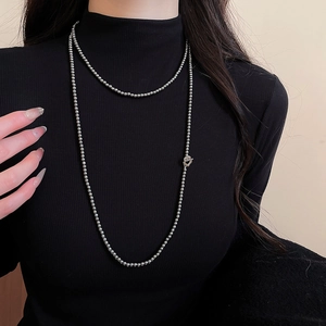 Macro detail of layered silver beaded necklace styled on a black sweater