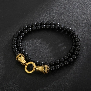 Detail of black double-layered beaded bracelet with two golden skull charms and ring clasp