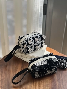 Macro detail of black fabric pouches with white floral embroidery and zipper closure