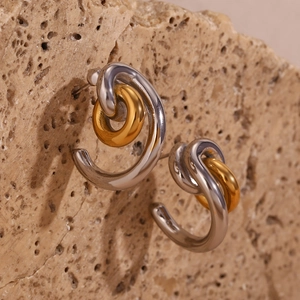 Detail of two-tone C-shaped hoop earrings with gold interlocking rings on stone surface