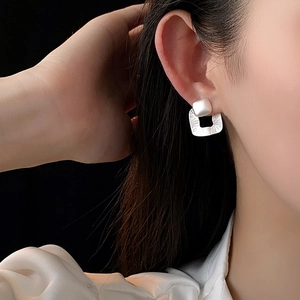 Close-up of textured silver square earrings worn by a model against a black background