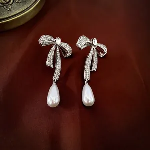 Bowknot pearl drop earrings with silver needles and rhinestones on dark satin