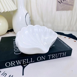 Dettaglio di un piatto per gioielli in ceramica a forma di conchiglia su un libro in stile minimal
