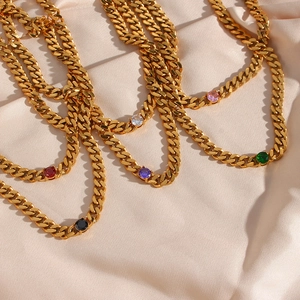 Flat lay of 18K gold plated Cuban chains with multi-colored round zircons on beige satin
