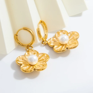 Detail view of gold flower earrings with white pearls on a minimalist background