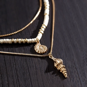 Detail shot of multi-layer gold chain necklace with white beads and seashell charms